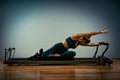 Young girl doing pilates exercises with a reformer bed. Beautiful slim fitness trainer on reformer gray background, low