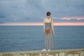 Young girl in a dress stands on a pier in the background of the sea and dark sky after sunset. Royalty Free Stock Photo