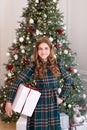 Young girl in dress stands with Xmas gifts in living room. Little girl opening magical christmas present at home. Portrait of beau