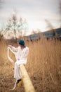 A young girl dressed in a white long dress, sitting on a pipe, near a wheat field. Behind her is a train