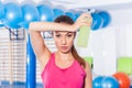 Young girl drinking isotonic drink, gym. She is wiping sweat Royalty Free Stock Photo