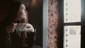 Young girl drinking tea from a mug and looking out the window sitting in modern loft dining 4k