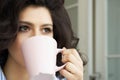 Young girl drinks coffee from a cup slooking into the distance.