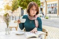 A young girl drinks coffee and reads a book in a restaurant