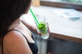 A young girl drinks a mojito through a straw while sitting in a cafe by the window. Royalty Free Stock Photo