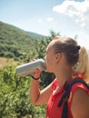 A young girl drinks water from a sports bottle outdoors on a blurred forest background. A woman quenches her thirst Royalty Free Stock Photo