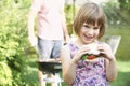 Young Girl Eating Beefburger At Family Barbeque