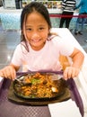 A young girl is eating Sizzling noodle in cast iron serving platters with egg, meats, seafood, vegetables, tofu, and noodles Royalty Free Stock Photo