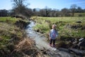A young girl enjoying herself wading in a stream, wearing Wellington boots and the weather is sunny.