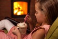 Young girl enjoying a hot chocolate in front of the fireplace