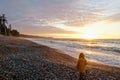 A young girl exploring a beach with the waves crashing to shore and the sun setting, on a beautiful evening on Agate Beach