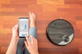 Young girl feet at home using a smart phone to control a round smart automatic vacuum, machine housework robot cleaning the floor