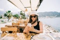 Young girl female lady in sunglasses looking at her mobile smart phone gadget in a street seaside cafe restaurant coffee