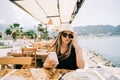 Young girl female lady in sunglasses looking at her mobile smart phone gadget in a street seaside cafe restaurant coffee