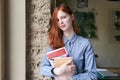 young girl female student with long red hair posing for a portrait with books in the hands with a relaxed confident expression