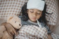 A young girl with a fever is lying in bed with a stuffed teddy bear Royalty Free Stock Photo