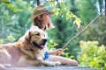 Young girl fishing while sitting with dog on pier Royalty Free Stock Photo