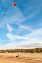 Young girl flying a kite while mother walks dog on a beach with blue sky in the background Royalty Free Stock Photo