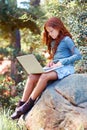 Young girl, forest and laptop on rock for internet, break and connection on holiday in woods for travel tips. Child, red Royalty Free Stock Photo