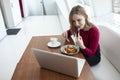 Young girl freelancer sits in a cafe with a laptop, drinks coffee and has breakfast, a student eats in the morning with a computer Royalty Free Stock Photo