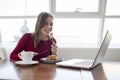 Young girl freelancer sits in a cafe with a laptop, drinks coffee and has breakfast, a student eats in the morning with a computer Royalty Free Stock Photo