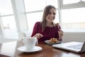 Young girl freelancer sits in a cafe with a laptop, drinks coffee and has breakfast, a student eats in the morning with a computer Royalty Free Stock Photo