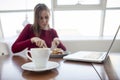 Young girl freelancer sits in a cafe with a laptop, drinks coffee and has breakfast, a student eats in the morning with a computer Royalty Free Stock Photo