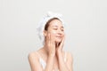 Young girl with fresh and clean skin, wearing white bath towel on her head, touching her face, looking with cute smile against Royalty Free Stock Photo