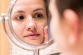 Young girl in front of a bathroom mirror putting cream on a red pimple. Beauty skincare and wellness morning concept Royalty Free Stock Photo