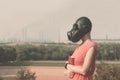 Young girl in a gas mask in a red dress with a book in her hands against the background of smoking factory chimneys on the horizon