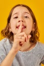 Young Girl Gesturing Silence With Finger on Lips Against Bright Yellow Background