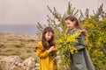 Retro young girl gives the elder sister mimosa on a green plateau near the sea in a storm Royalty Free Stock Photo