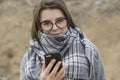 Young girl in glasses holds a phone in her hands on the background of a sand pit