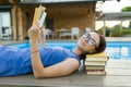 Young girl in glasses near the pool with a pile of books, reading book. Education, summer, knowledge.