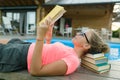 Young girl in glasses near the pool with a pile of books, reading book. Education, summer, knowledge.