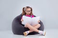 Young girl in glasses reading a book on a gray bean bag Royalty Free Stock Photo