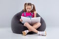 Young girl in glasses reading a book on a gray bean bag Royalty Free Stock Photo