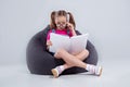 Young girl in glasses reading a book on a gray bean bag Royalty Free Stock Photo