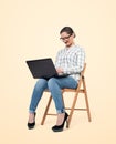 A young girl in glasses, shirt and jeans is sitting on a chair and working on a laptop, on a bright yellow background