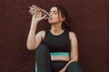 A young girl goes in for sports on the street and drinks water while sitting near the wall