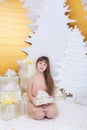 Young girl in golden dress laughs and enjoys gift. Little girl opening magical christmas present at home. child holds christmas pr
