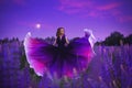 A magical portrait of a young girl in a gradient dress in a purple-pink lupine field at night. Royalty Free Stock Photo