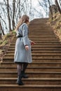Young girl in gray coat climbs stairs in park in autumn