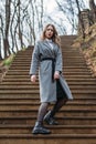 Young girl in gray coat posing on stairs in park on an autumn sunny day