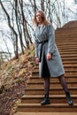 Young girl in gray coat posing on stairs in park on an autumn sunny day