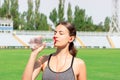Young girl in gray sportswear drink water and listening music after teaining. woman standing and drinking with bottle at stadium. Royalty Free Stock Photo