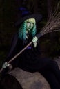 Young girl with green hair and broom in suit of witch in forest. Halloween time Royalty Free Stock Photo