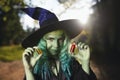 Young girl with green hair and skin suit of witch in forest holds small bottles with red and orange potion. Halloween time