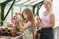 Young girl in greenhouse watering plant with woman