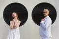 Young girl and guy are sitting against background of black round windows of portholes